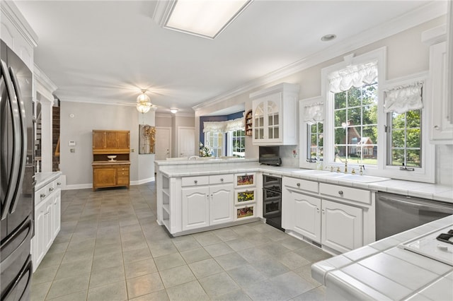 kitchen with a sink, tile counters, freestanding refrigerator, a peninsula, and white cabinetry
