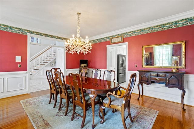 dining room featuring an inviting chandelier, ornamental molding, stairs, wainscoting, and light wood-type flooring