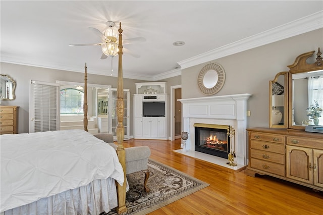 bedroom with light wood-style floors, ornamental molding, and a glass covered fireplace