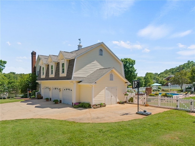 view of side of property with a garage, fence, a chimney, concrete driveway, and a yard