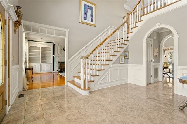 foyer entrance with visible vents, a towering ceiling, stairway, marble finish floor, and a decorative wall