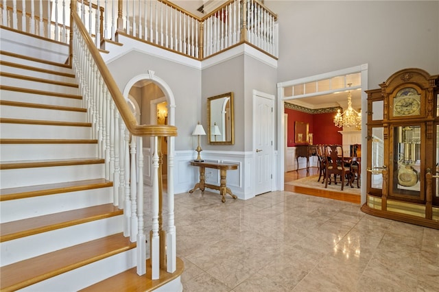 stairway featuring a towering ceiling, wainscoting, a notable chandelier, ornamental molding, and a decorative wall