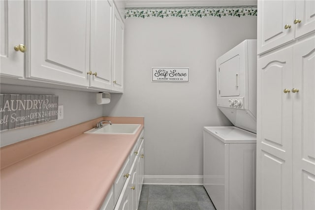 laundry area featuring cabinet space, a sink, baseboards, dark tile patterned floors, and stacked washer and clothes dryer