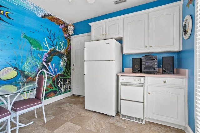 kitchen featuring freestanding refrigerator, white cabinetry, stone finish floor, and light countertops
