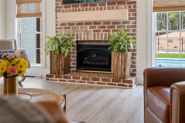 living room with a brick fireplace, a wealth of natural light, and wood finished floors