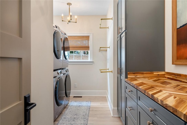 clothes washing area with cabinet space, an inviting chandelier, light wood-style floors, baseboards, and stacked washer and clothes dryer