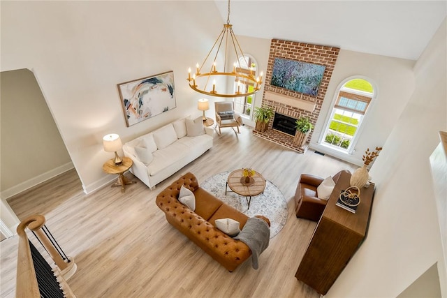 living room with an inviting chandelier, baseboards, a brick fireplace, and wood finished floors