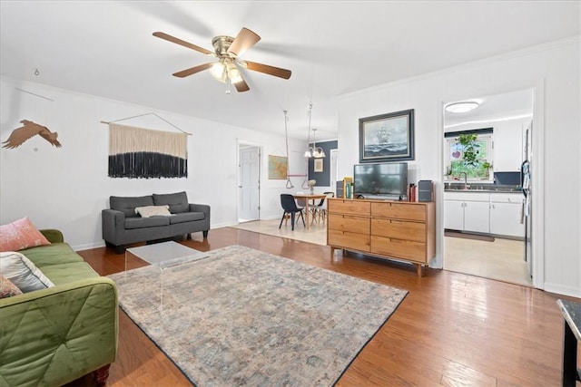 living area with crown molding, a ceiling fan, and wood finished floors