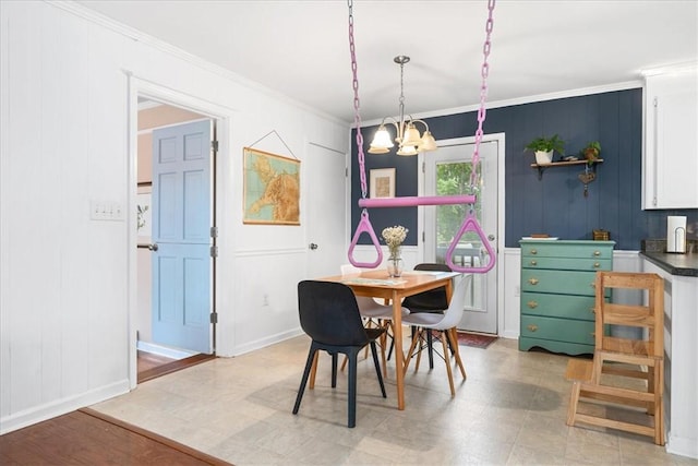 dining area with baseboards, ornamental molding, a decorative wall, and a notable chandelier