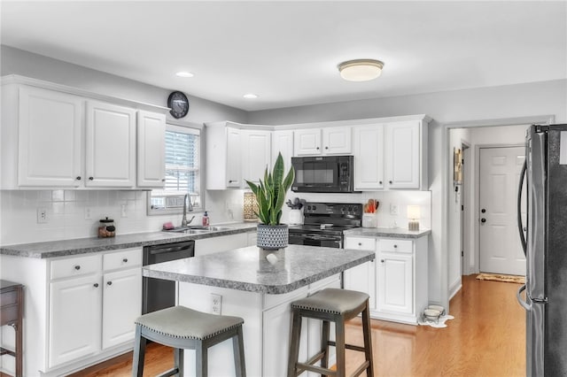 kitchen featuring a breakfast bar area, white cabinets, a sink, light wood-style flooring, and black appliances