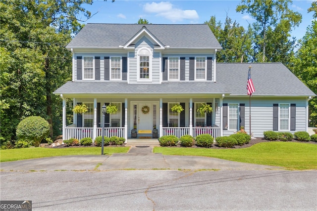 colonial inspired home featuring roof with shingles, covered porch, and a front yard