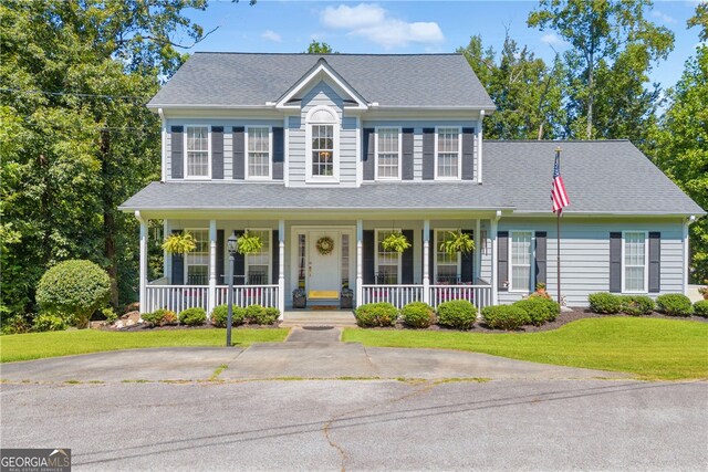 colonial house featuring a front lawn, roof with shingles, and covered porch
