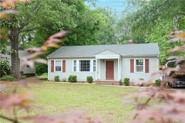 ranch-style home with roof with shingles, a chimney, and a front lawn