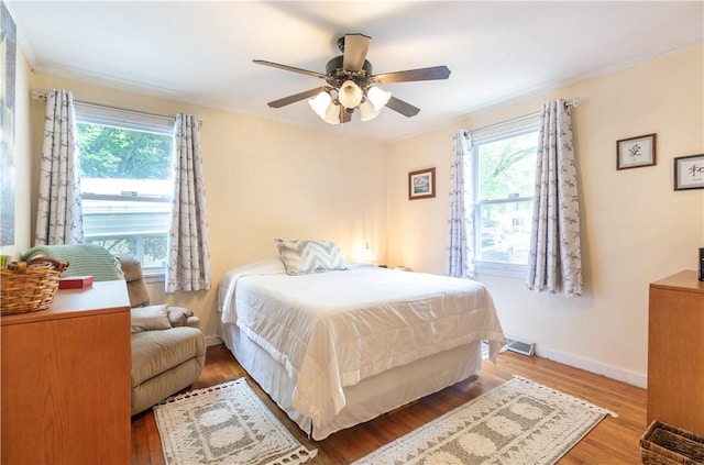 bedroom featuring ornamental molding, wood finished floors, and multiple windows