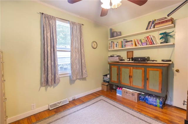 interior space with a ceiling fan, baseboards, wood finished floors, visible vents, and ornamental molding