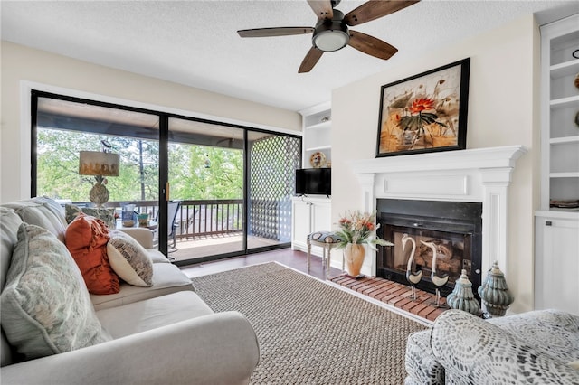living room with ceiling fan, a glass covered fireplace, built in shelves, and plenty of natural light