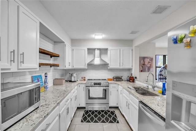 kitchen featuring wall chimney range hood, appliances with stainless steel finishes, open shelves, a sink, and white cabinetry