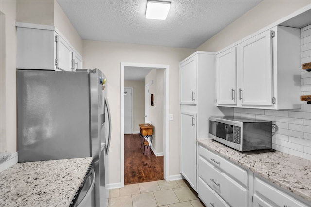 kitchen with decorative backsplash, light stone countertops, a textured ceiling, white cabinets, and stainless steel appliances
