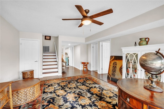 interior space with a ceiling fan, visible vents, baseboards, stairs, and dark wood-type flooring