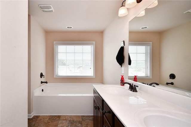 bathroom with a sink, a bath, double vanity, and visible vents