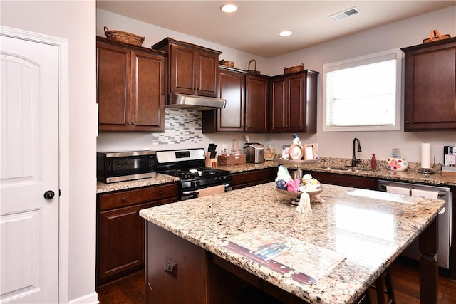 kitchen with light stone counters, a sink, stainless steel appliances, under cabinet range hood, and visible vents