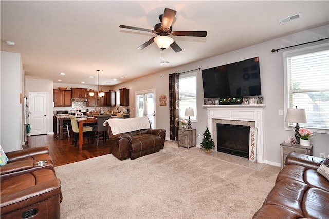 living area featuring ceiling fan with notable chandelier, dark colored carpet, recessed lighting, a high end fireplace, and visible vents