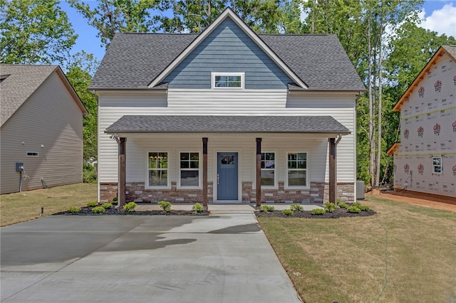 craftsman inspired home featuring a porch, cooling unit, a shingled roof, and a front lawn