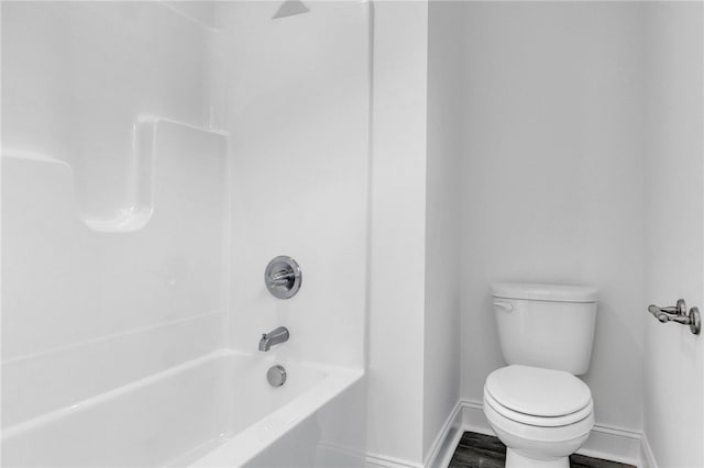bathroom with baseboards, wood finished floors, bathing tub / shower combination, and toilet