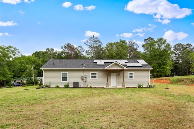 rear view of house with roof mounted solar panels, central air condition unit, and a yard