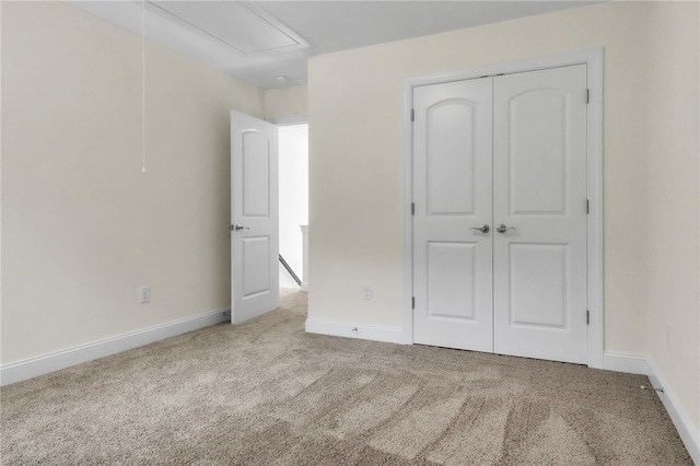 unfurnished bedroom with baseboards, carpet, attic access, and a closet