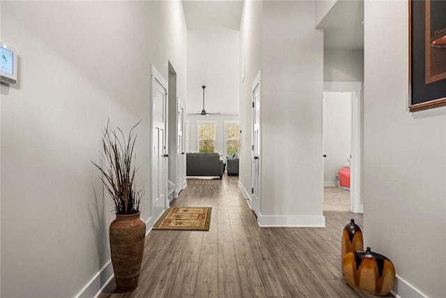 corridor with baseboards, wood finished floors, and a towering ceiling