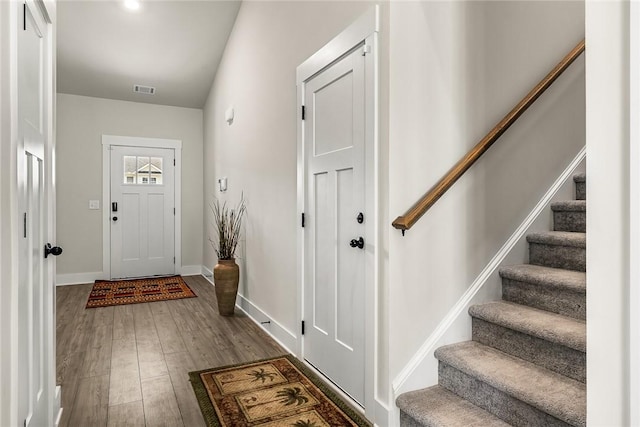 foyer entrance with baseboards, visible vents, wood finished floors, and stairway