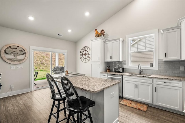 kitchen featuring stainless steel dishwasher, backsplash, a sink, and lofted ceiling