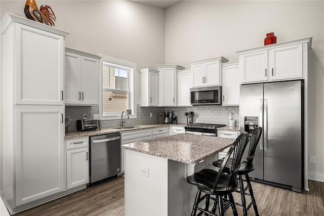 kitchen featuring a center island, wood finished floors, a sink, a high ceiling, and stainless steel appliances