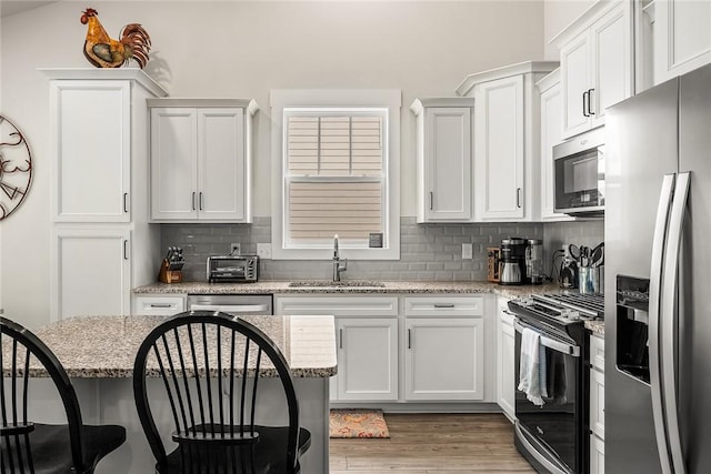kitchen featuring a kitchen breakfast bar, decorative backsplash, appliances with stainless steel finishes, a sink, and white cabinetry