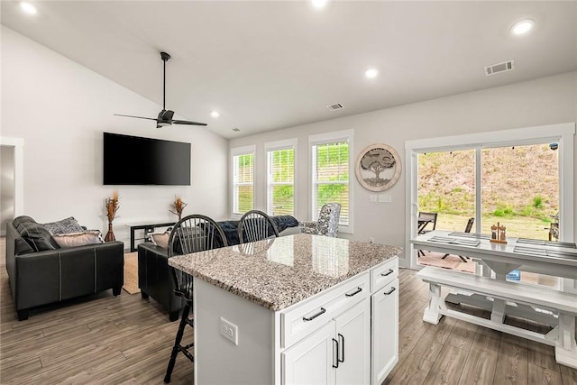 kitchen with visible vents, open floor plan, a kitchen breakfast bar, light wood-type flooring, and a ceiling fan