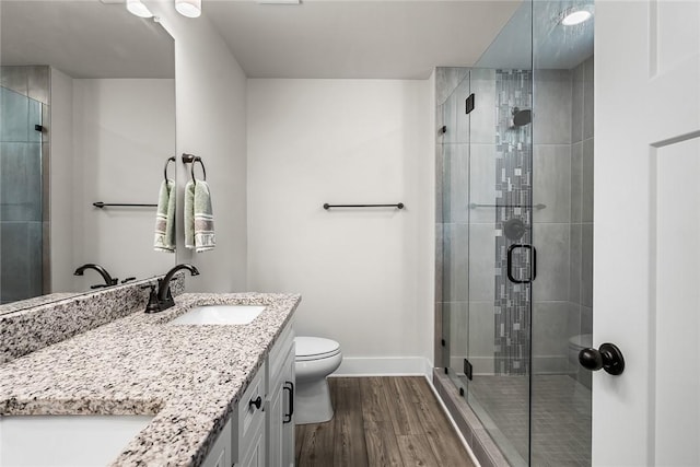bathroom featuring a stall shower, wood finished floors, vanity, baseboards, and toilet