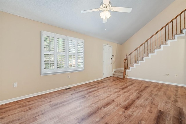 unfurnished living room featuring ceiling fan, vaulted ceiling, stairway, baseboards, and light wood-style flooring