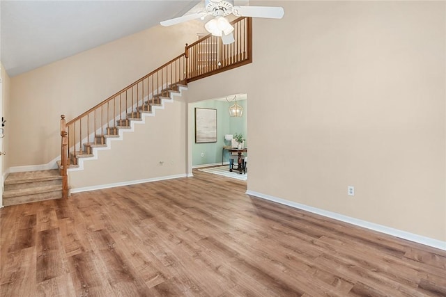 unfurnished living room with a towering ceiling, wood finished floors, stairway, and ceiling fan with notable chandelier