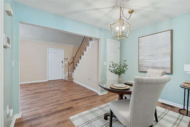 dining space with visible vents, wood finished floors, stairway, baseboards, and a chandelier