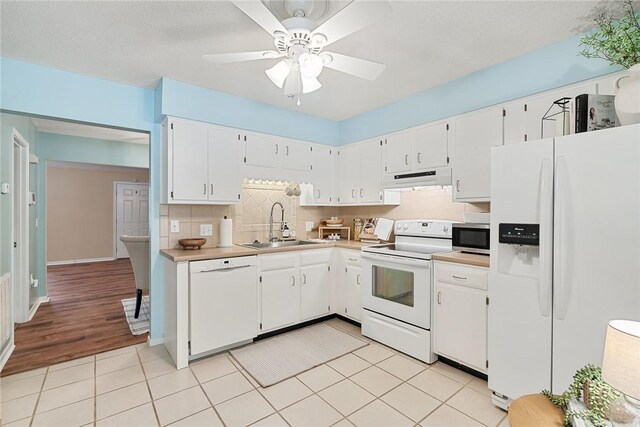 kitchen with a sink, tasteful backsplash, under cabinet range hood, and white appliances