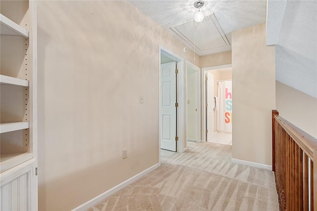 hallway with a textured ceiling, baseboards, light carpet, and attic access