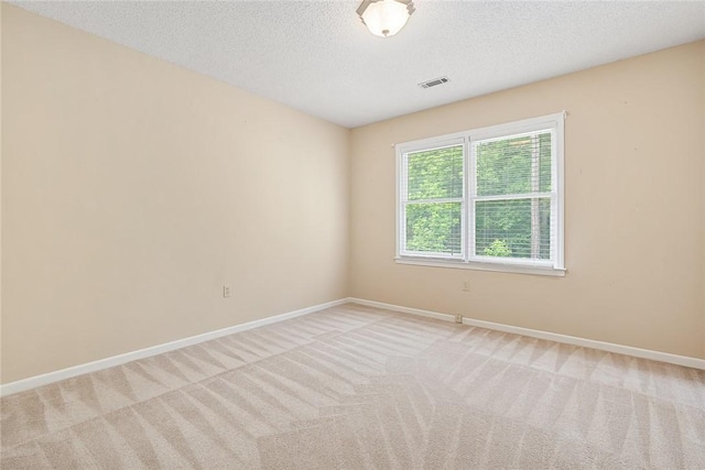 spare room with visible vents, a textured ceiling, baseboards, and light colored carpet