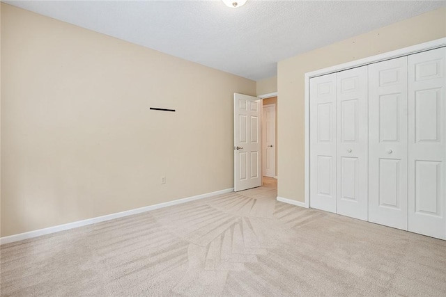 unfurnished bedroom with light colored carpet, a textured ceiling, baseboards, and a closet