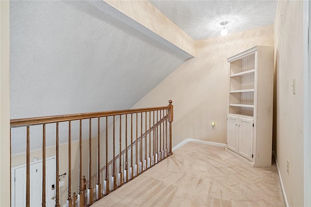 corridor featuring a textured ceiling, vaulted ceiling, baseboards, an upstairs landing, and carpet