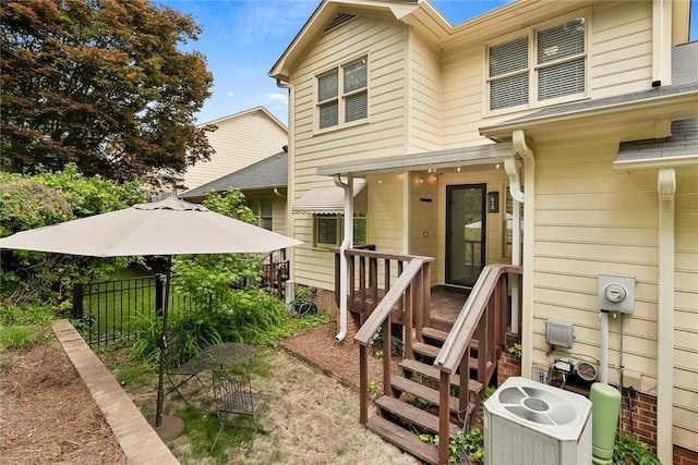 view of exterior entry with central AC, a wooden deck, and fence
