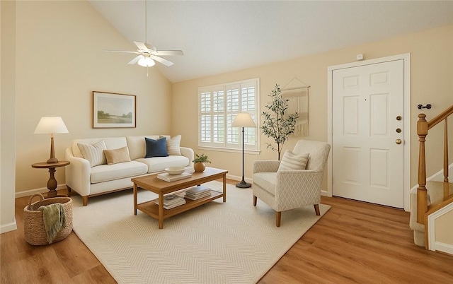 living area with light wood-type flooring, a ceiling fan, vaulted ceiling, and stairway