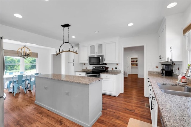 kitchen with white cabinets, dark wood-style flooring, a sink, stainless steel appliances, and a kitchen island