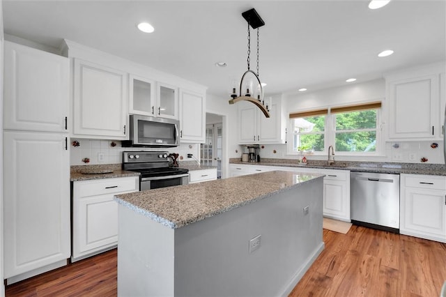 kitchen with appliances with stainless steel finishes, tasteful backsplash, light stone countertops, light wood finished floors, and white cabinetry