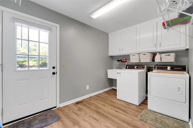 clothes washing area featuring visible vents, baseboards, cabinet space, separate washer and dryer, and light wood-style flooring